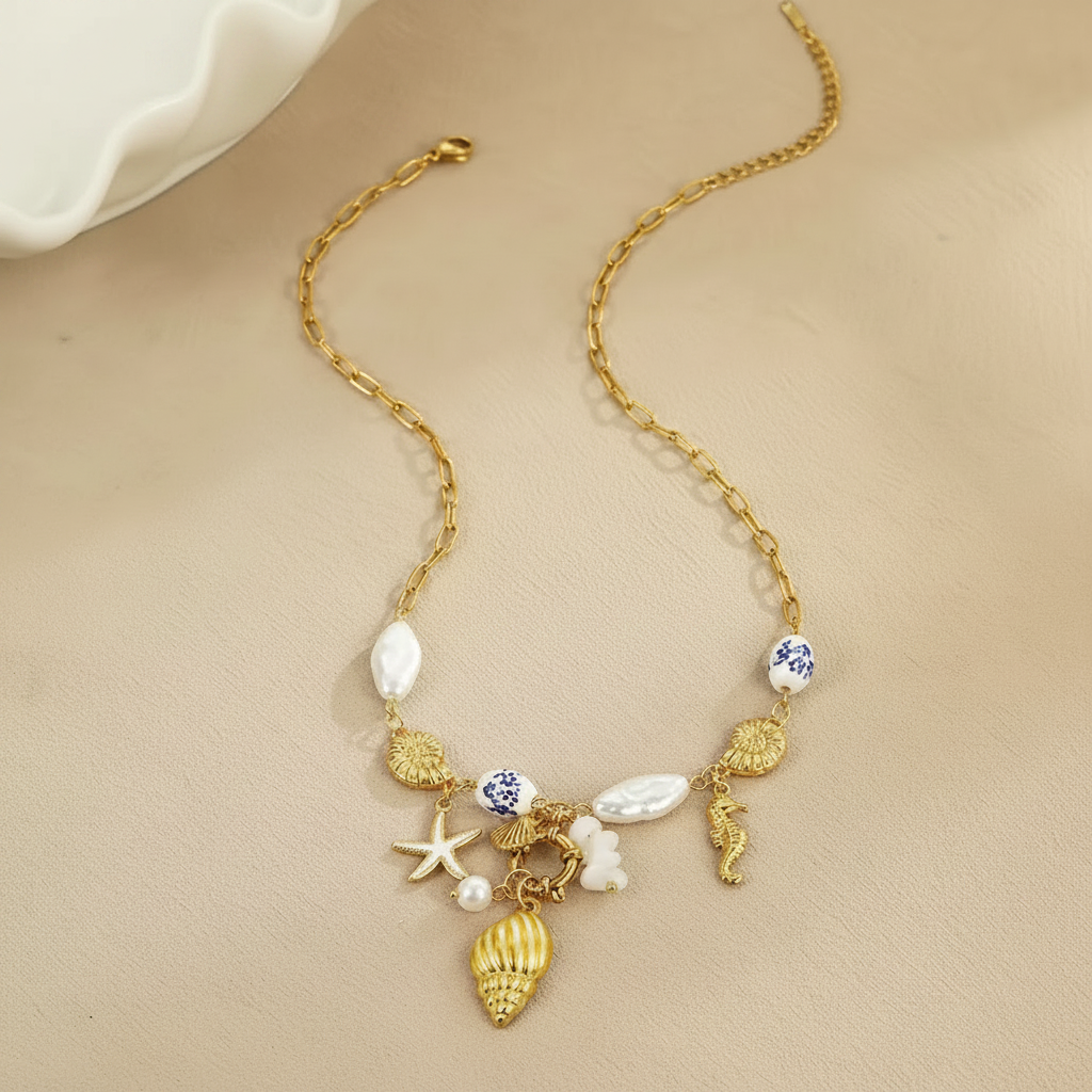 Collier doré avec perles baroques, céramique bleu et blanc et breloques marines sur fond beige
